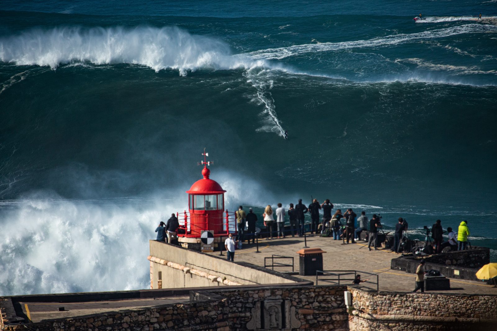 Surfer riding a large wave near a crowded lookout