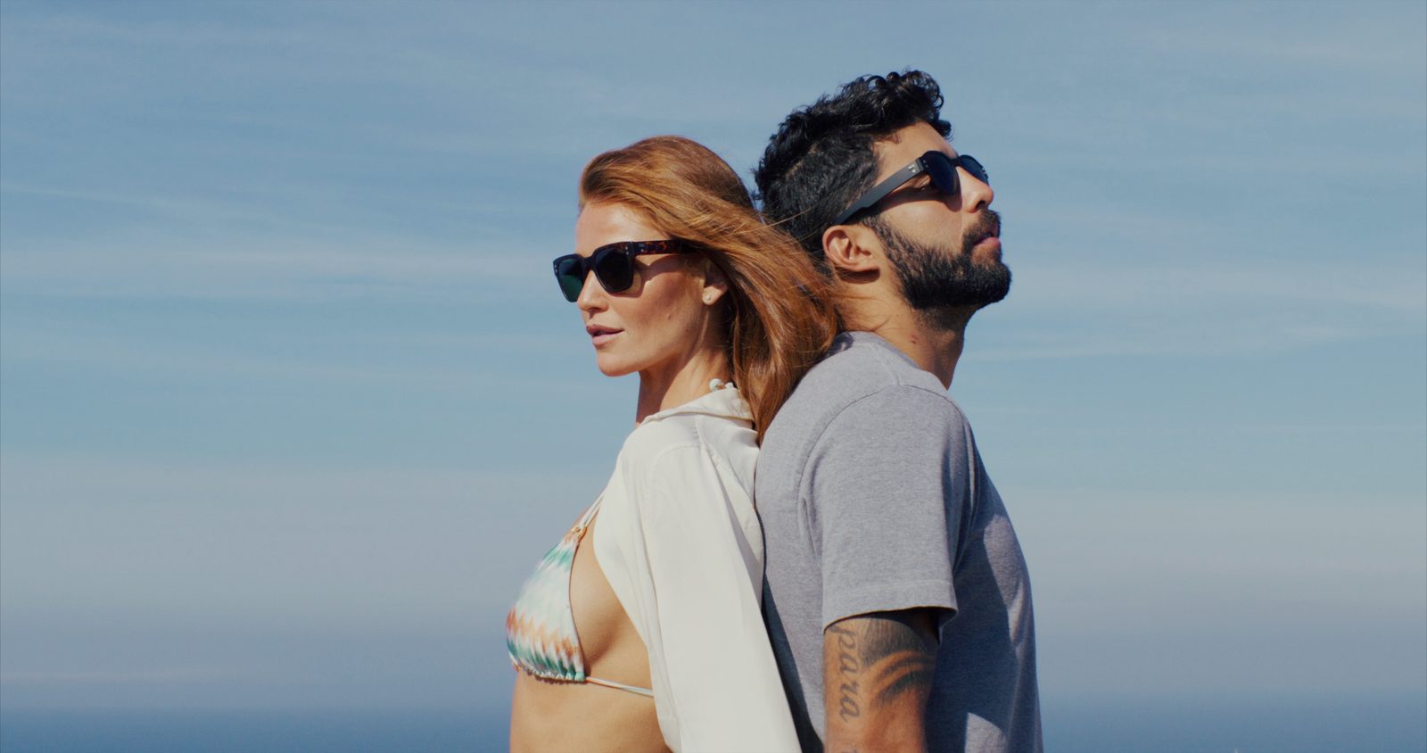 Two people wearing sunglasses standing beside the sea